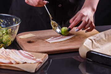 young woman wraps Brussels sprouts into bacon