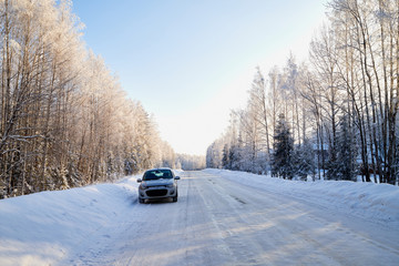 White snow road with car amoung winter trees in forest in a sunny day