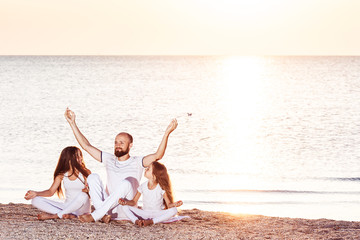 family at dawn doing yoga or meditation on beach.