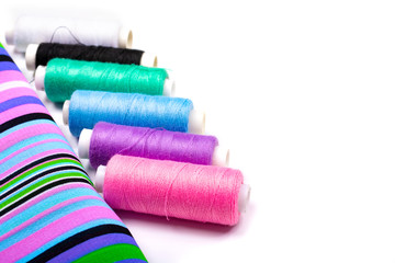 Sewing. Background of striped fabric and spools of threads of different colors on a white background. Side view, space for text, Copy space,