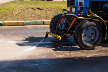 Blue tractor watering asphalt for cleaning dust and dirt.  Summer road cleaning