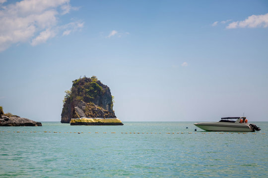 The rock in the andaman sea is painted with gold paint. Thai spirituality. Speedboat floats nearby. Blue sky, a lot of clouds. Cave beach. Pranang, Krabi province