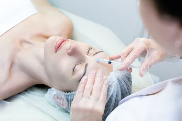 Obraz na płótnie Canvas Beauty injection for female face. Cosmetician sets filler in forehead, close up, selected focus