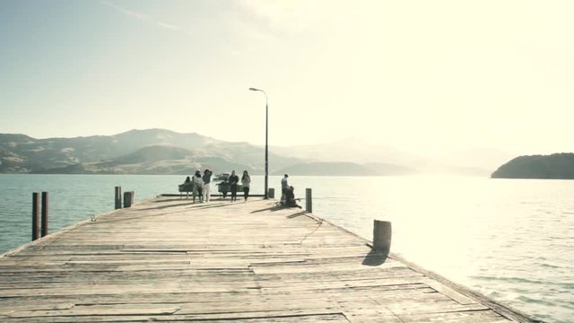 People are walking down pier in summer, bright blue water in popular tourist town Akaroa, Christchurch, New Zealand, Sun is shining in summertime