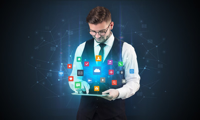Handsome businessman in suit with tablet on his hand and application icons above
