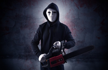 Armed rude assassin in an empty bloody room concept with gun ax chainsaw mallet wrench
