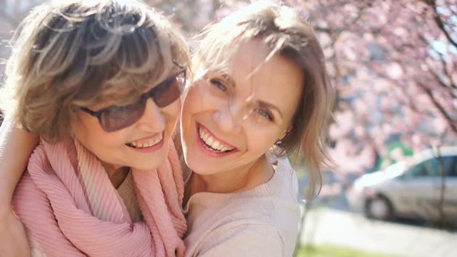 Beautiful sunny spring portrait of mother and daughter. Two women hugging and laughing against the backdrop of sun glare and flowering trees