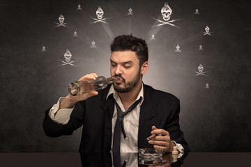 Loser drunk man sitting at table with skulls concept around
