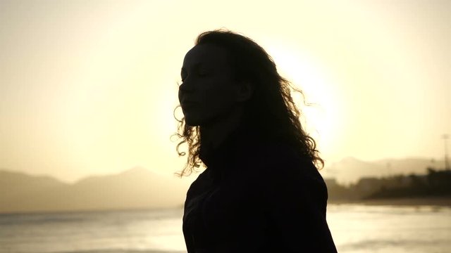 Slow Motion Close up silhouette of Young Woman moving her head with hair blowing in wind looking at sunset over ocean.