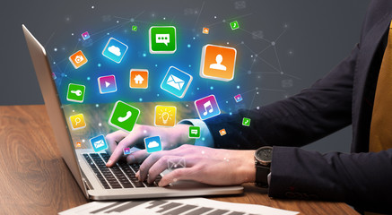 Businessman hand typing on laptop with flying application icons around
