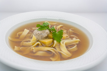 Traditional European transparent beef noodle soup with potatoes and wheat dressing with parsley in a white plate in a restaurant