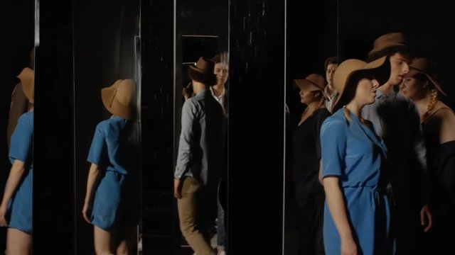 Group of young people randomly walking around the room through the mirrors. Company of singers on a black background with mirrors. Concept of space and time