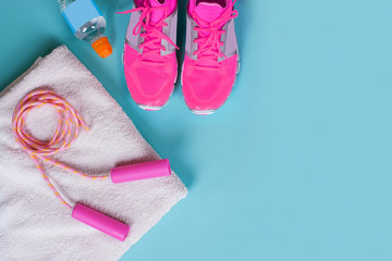 Flat lay of blue dumbbell, running sneaker, towel, sport equipments, fitness items, top view. over blue background.