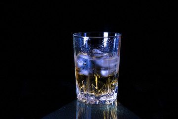 Cold glass of whiskey with ice, in blue tones, covered with hoarfrost, stands in the dark on granite glass