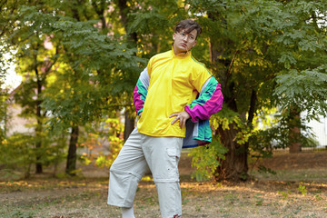 Young handsome caucasian man with bright freaky sportswear 70s style stands at a morning park....