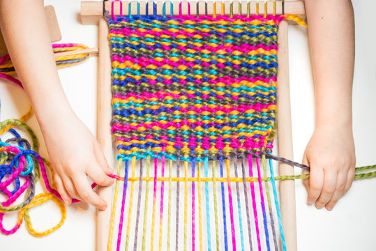 Weaving. Hands of little caucasian girl working on small loom weaving.