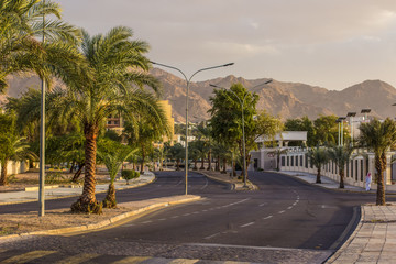 Arabian city street Aqaba in Jordan Middle East environment palm tree and mountain horizon environment, empty road and dramatic cloudy weather before sunset 
