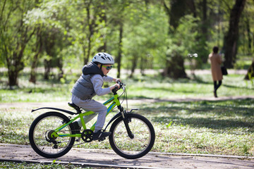 Little boy learns to ride a bike in the park. Cute boy in sunglasses rides a bike. Happy smiling child in helmet riding a cycling.