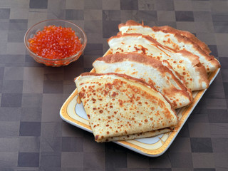 Four ruddy pancake neatly on the plate. Next to the bowl with red caviar. Nutritious healthy food with vitamins and minerals. Breakfast, lunch or dinner fried pancake with caviar of red fish. Close up