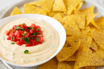 Homemade cheesy dip in a bowl, yellow tortilla chips, side view. Close-up.