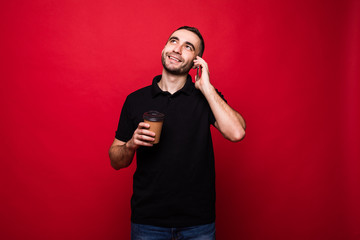 Handsome man with coffee cup to go talk on phone on red background