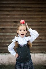 Portrait of a happy school girl with two big white bows in their hair standing with red apple on head.