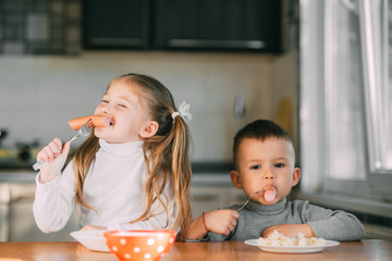 Boy and girl children in the kitchen eating sausages with pasta is very fun and friendly