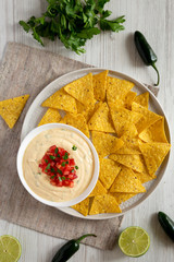 Top view, homemade cheesy dip with yellow tortilla chips over white wooden background. Flat lay,...