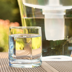 Water filter pitcher and a clean glass of a clear water close up on the summer garden background