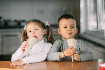 kids boy and girl eating ice cream cone in the kitchen is a lot of fun