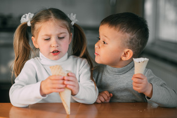 kids boy and girl eating ice cream cone in the kitchen is a lot of fun