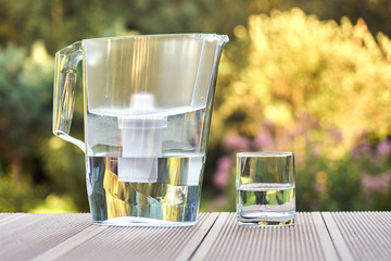 Water filter pitcher and a clean glass of a clear water close up on the summer garden background