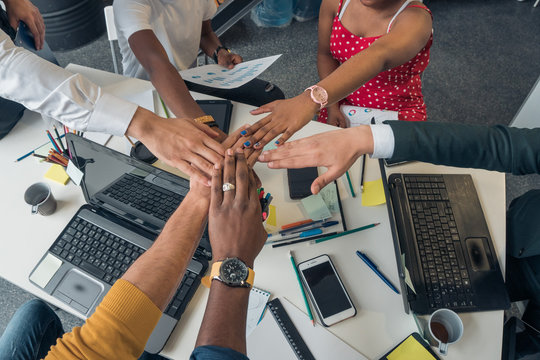 Young people of different nationalities hold a meeting in a modern stylish office. Partners folded his hands in a sign of friendship.