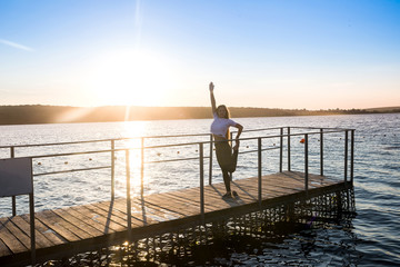 Fototapeta premium An active young woman stands on berth of lake at sunrise