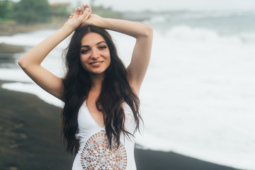 Fototapeta na wymiar Portrait of happy girl with beautiful smile in swimsuit posing on black sand beach