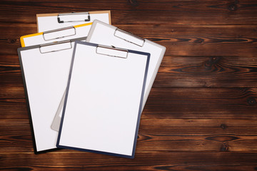 Clipboard with white sheet on wood background. Top view.