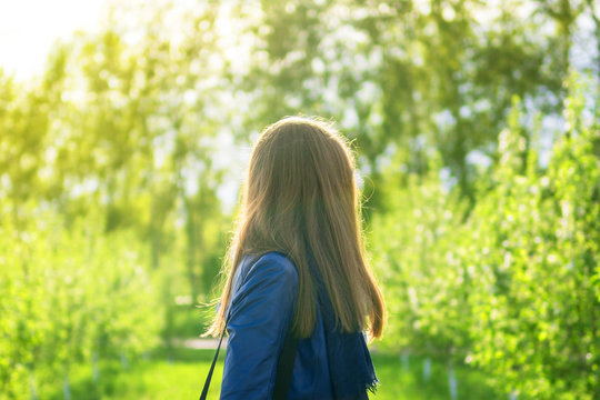 young girl walks in the park on a summer sunny day - a view from behind 
