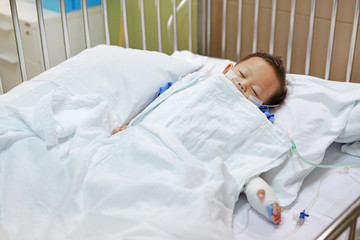 Baby boy sleeping with attaching intravenous tube to hand on bed at hospital. Baby admitted at...