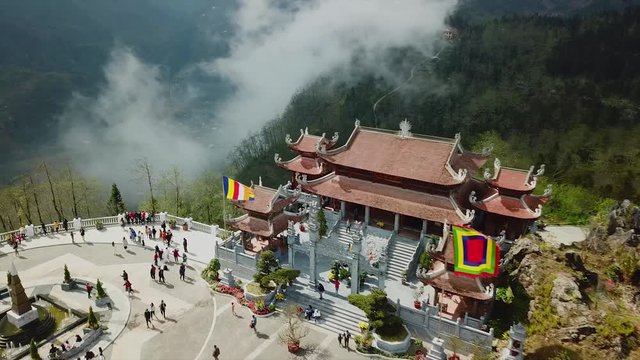 Aerial forward descent Chinese temple Buddhism sun world Fansipan territory high mountains in clouds landscape Vietnam Sapa. People tourists walk. Sunny day Asian style authentic culture spruce forest