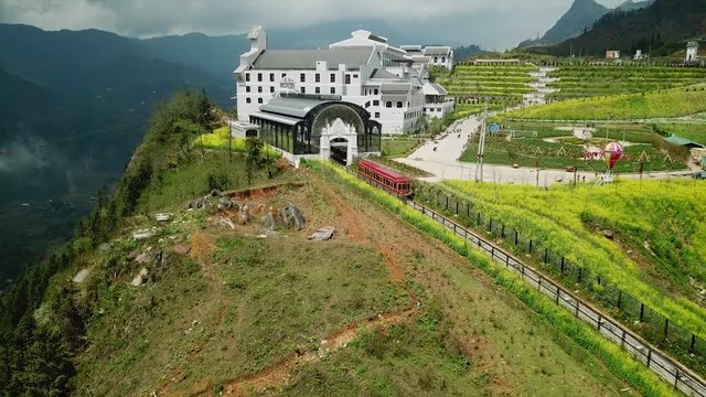 Epic overall railway red wagon rides into station on top of mountain. Modern french style building World Fansipan cable road funicular Sapa Vietnam landmark. Tourism Travel. Helicopter 