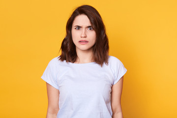 Obraz premium Brunette woman in casual clothes expressing disgust, dislikes something, having tensive look frowning face. Cauasian woman with pleasant appearance looking posing isolated over yellow background.