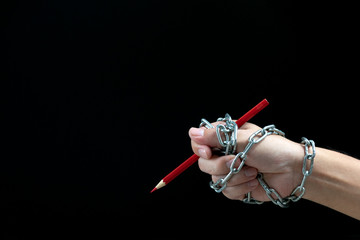 Hand with red pencil tied with fetters, depicting the idea of freedom of the press or freedom of...