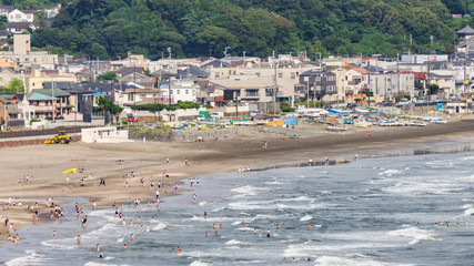 Panoramic aerial view on the seaside of Kamakura from top of a hill. People enjoying weekend: sun bathing, swimming in ocean, relaxing. Breathtaking landscape seen on a summer day in Kanagawa, Japan