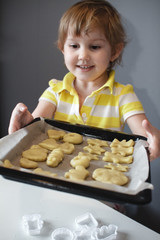 A little girl holding a baking sheet with cookies, shows the camera