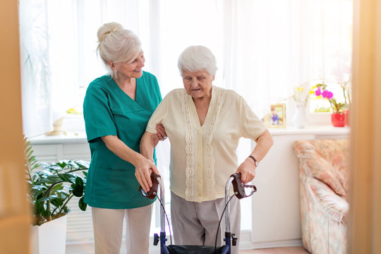 Nursing assistant helping senior woman with walking frame