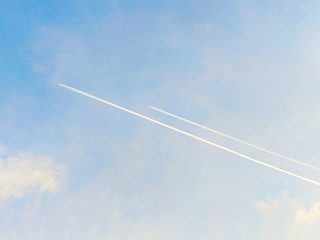 Airplanes flying with trail in the blue sky among clouds and sunlight.