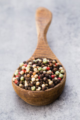 Peppercorn mix in a wooden bowl on grey table.