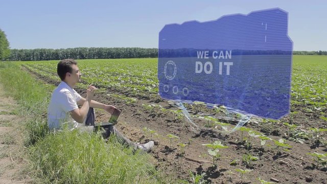 Man is working on HUD holographic display with text We can do it on the edge of the field. Businessman analyzes the situation on his plantation. Scientist examines future technology