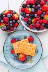 Homemade waffles with berries salad on blue dishes. Vintage wooden background.