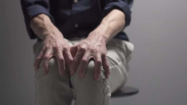 A man is sitting on a chair nervous. Seems like he is having a panic attack.